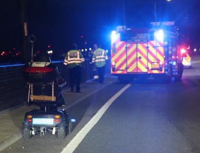 Mobility scooter on the side of a road at night, emergency services in the background.