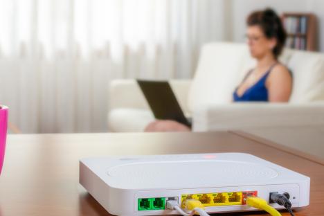 Wifi router with ethernet cables connected, woman using laptop in background.
