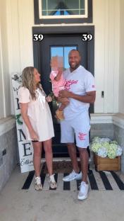 A pregnant woman, a man, and a toddler stand on their porch.