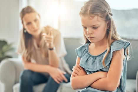 Upset young girl with arms crossed being scolded by her mother.