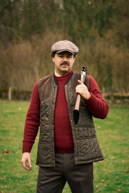 Man in a vest and flat cap carrying a shotgun.