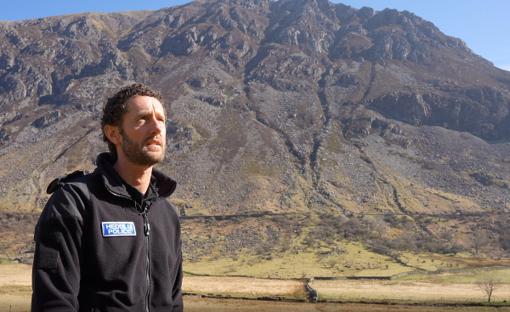Mountain rescue volunteer in uniform against mountain backdrop.