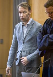 A man in a light blue blazer stands in a courtroom.