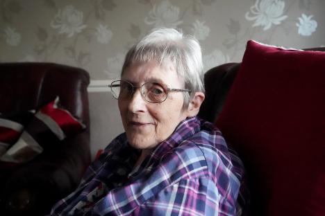 Portrait of an elderly woman wearing glasses and a plaid shirt.