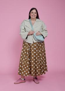 Woman in polka dot skirt and beige jacket with a light blue crossbody bag.