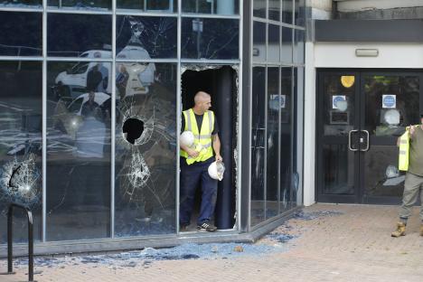 A man in a safety vest surveys damage to the windows of a building.