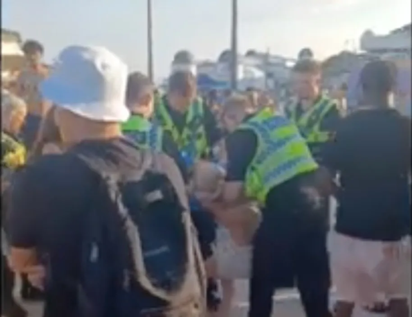 Police officers detaining a person in a crowd.