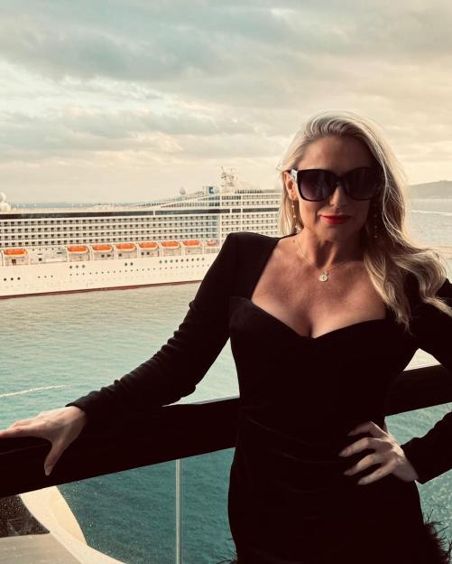 Woman in black dress on a balcony overlooking a cruise ship.