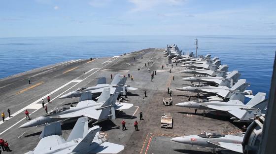 Aircraft carrier flight deck with numerous fighter jets.
