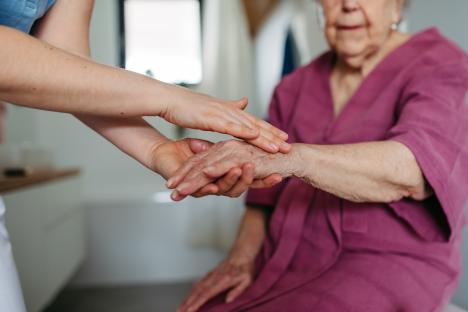 Home caregiver applying lotion to elderly woman's hands.