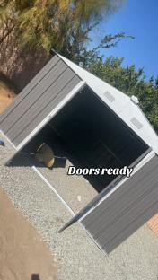 Grey metal storage shed with doors open.