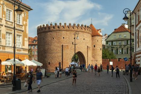 Brick gate in Warsaw's New Town with people walking by.