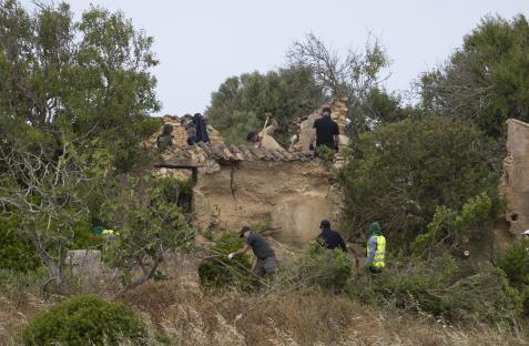 Police searching scrub land near an abandoned building.