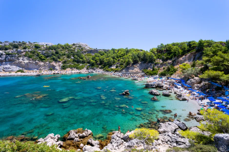Beach cove with crystal-clear turquoise water and many people swimming and sunbathing.