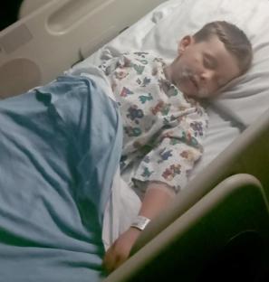 Young boy sleeping in a hospital bed with injuries.