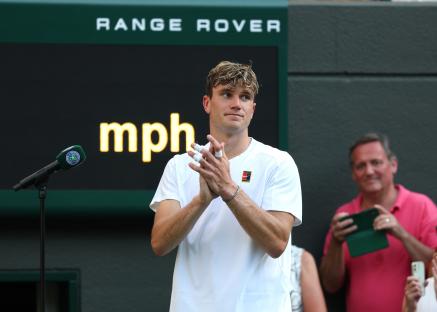 Jack Draper applauds the crowd at Wimbledon after his opponent retires due to injury.