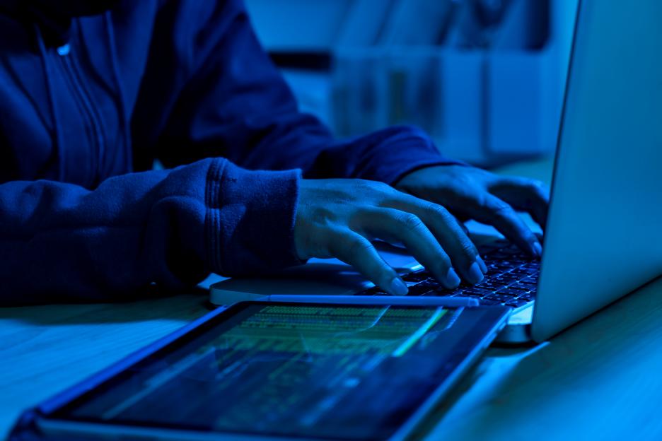 Person using laptop and tablet to code, possibly for malicious purposes.