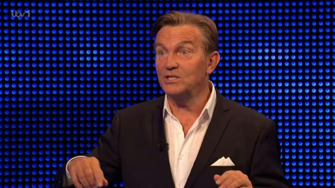A man in a suit speaking in front of a blue background.