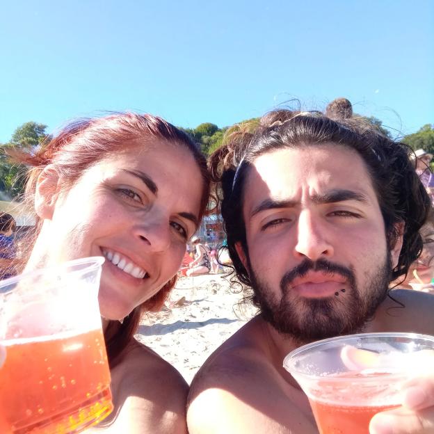 Couple toasting with drinks on a beach.