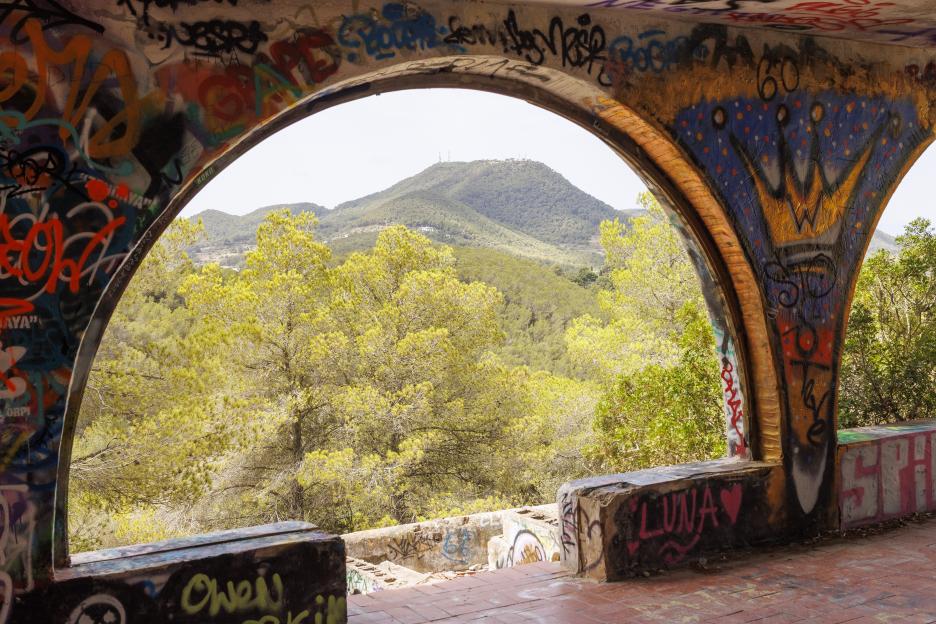 Graffiti-covered arches frame a view of a hillside.