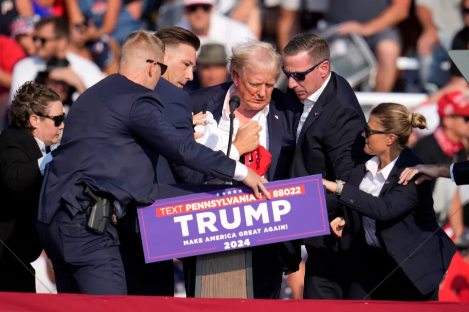 Donald Trump being assisted by security personnel at a rally.