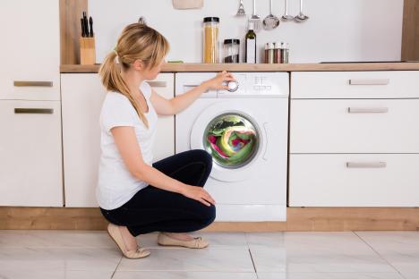Woman crouching by washing machine, adjusting settings.