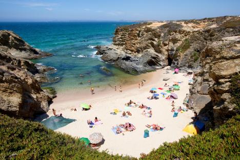 Beach cove in Porto Covo, Alentejo, Portugal with people sunbathing.