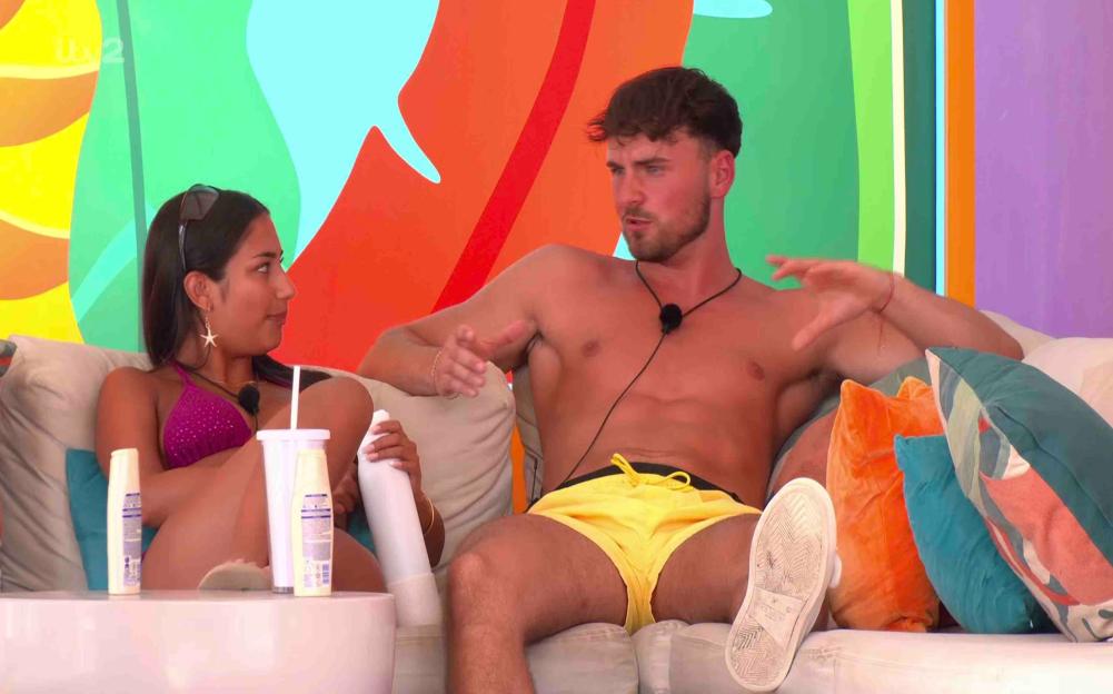 A man and woman sit on a couch and talk.