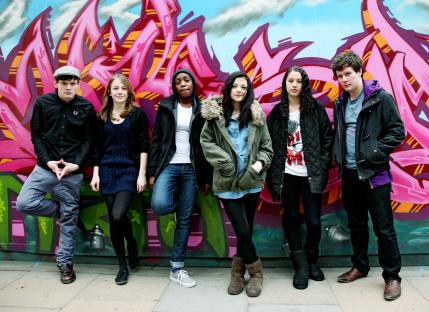 Six young adults posing in front of a graffiti wall.