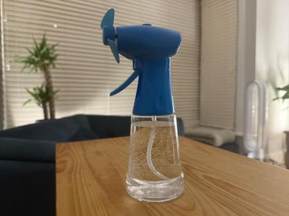 Spray bottle with a small fan attached, sitting on a wooden table.