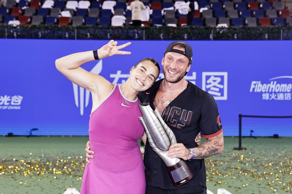 Aryna Sabalenka and her coach posing with a trophy after a tennis match.