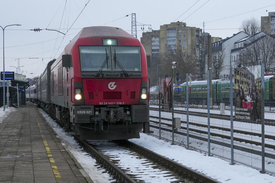 A red train at a station with a photo exhibition about the war in Ukraine visible through the train windows.