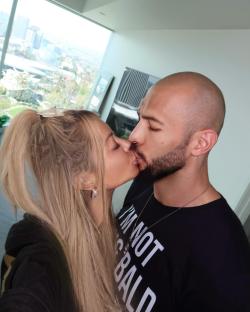 Couple kissing in front of a window with a city view.