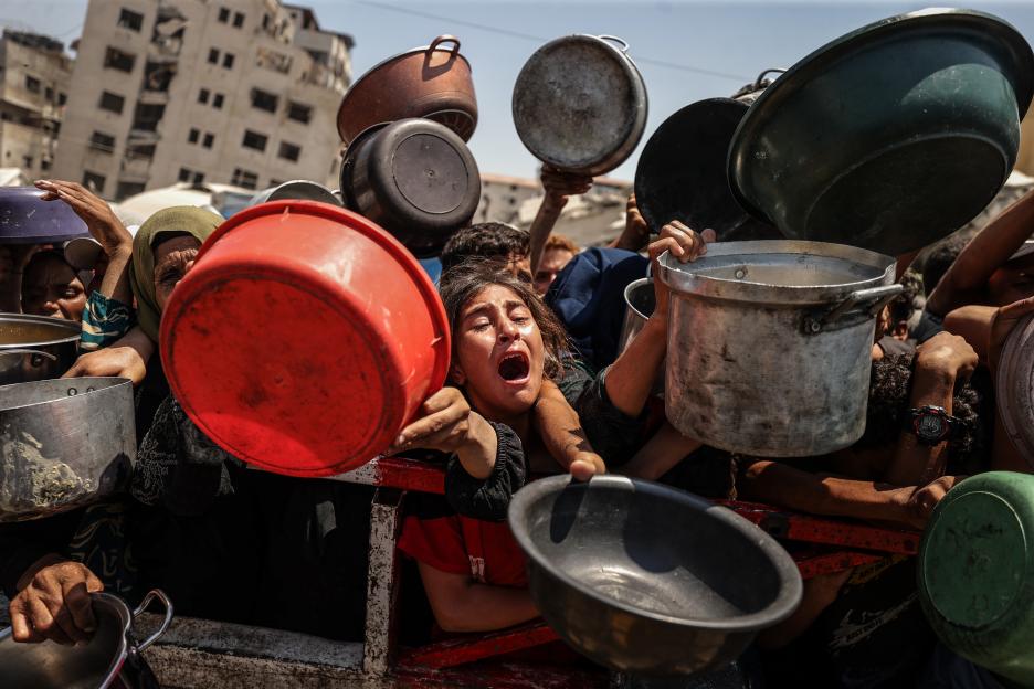 Palestinians holding out bowls and pots to receive food during a food shortage.