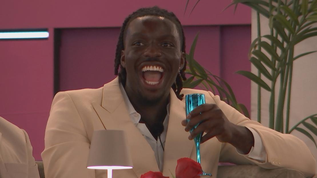 A man in a cream blazer laughs while holding a teal glass.
