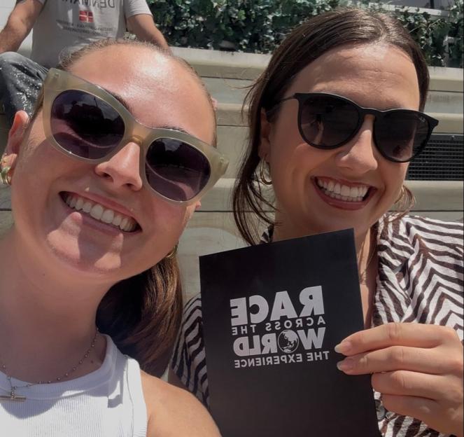 Two women holding a Race Across the World Experience pamphlet.