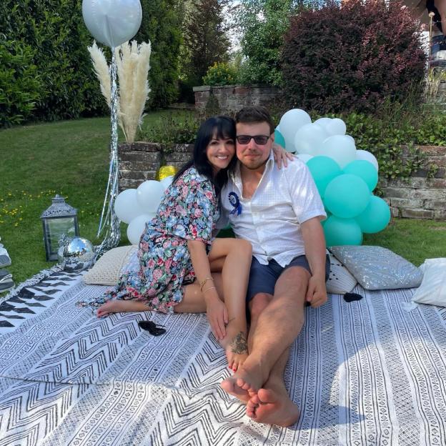 Couple sitting on a blanket outdoors with balloons.