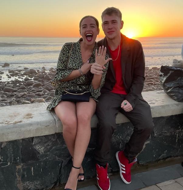 A couple showing off an engagement ring at sunset by the ocean.