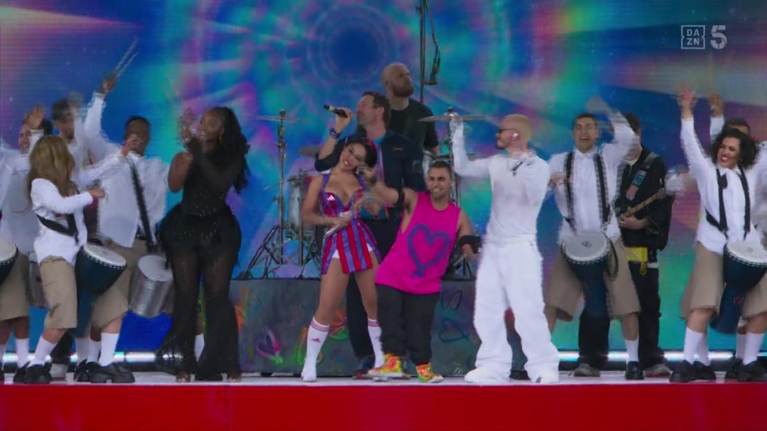 Band performing on stage with drummers and singers.