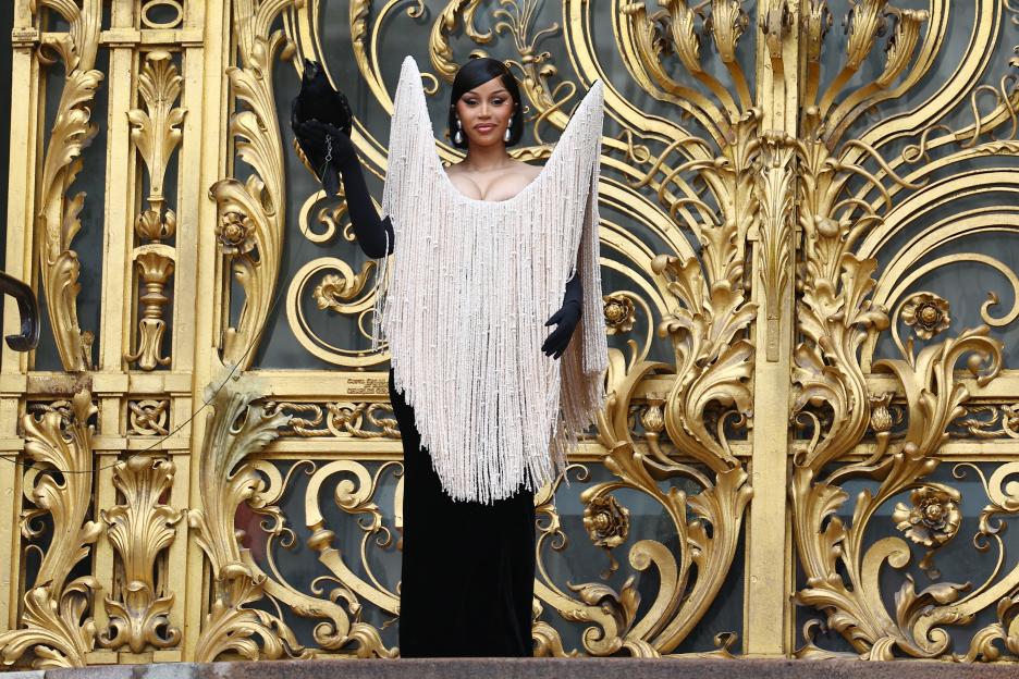 Cardi B holding a black bird, wearing a beaded gown at a fashion show.