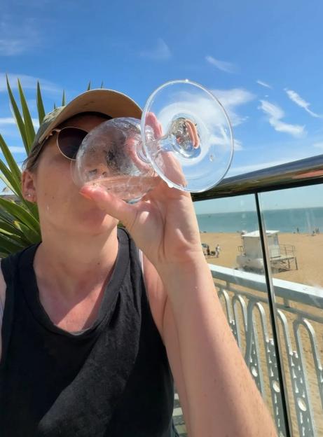 Person drinking from a wine glass outdoors overlooking a beach.