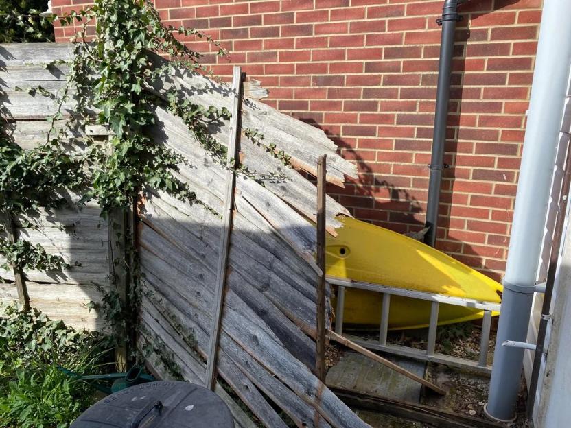 Broken fence with ivy growing on it, and a yellow kayak leaning against it.