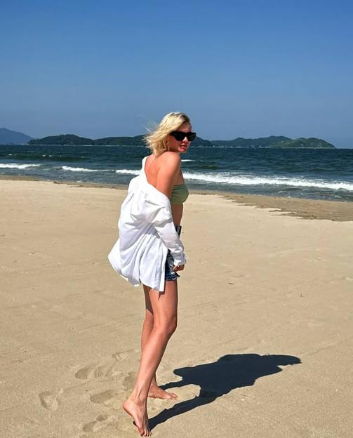 Woman in sunglasses and a bathing suit walking on a beach.
