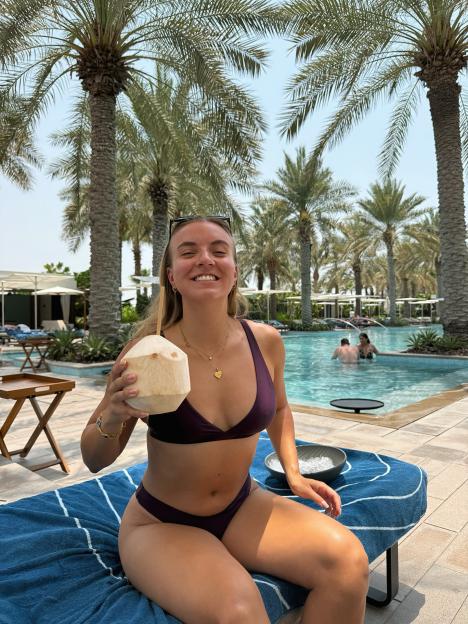 Woman in a purple bikini drinking coconut water by a pool.