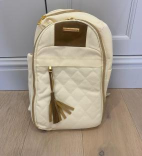 Cream-colored quilted backpack with gold zippers and brown tassel.