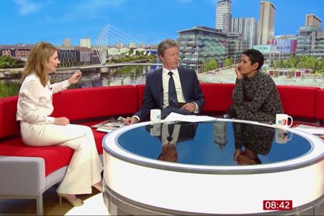 Three people sitting on a red sofa during a television interview.