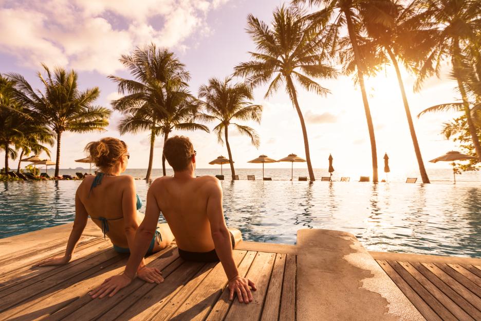Couple relaxing by a resort pool at sunset.