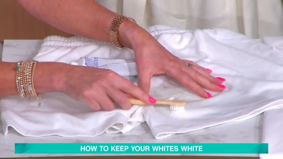 Screenshot of a person using toothpaste and a toothbrush to remove a stain from white clothing.