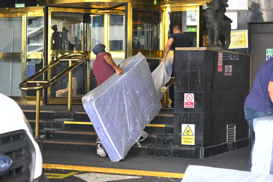 Two men carrying mattresses into a hotel.