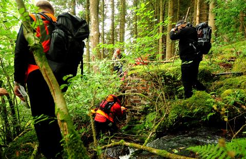 Police and mountain rescue teams searching a wooded area for a missing person.